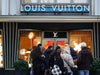 Vetrina Louis Vuitton con insegna del marchio e passanti davanti al negozio